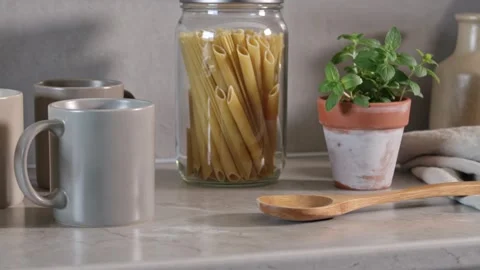 Still life scene on a modern kitchen countertop with pasta, mugs, and a potted Vidéo 335786228