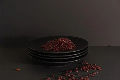 Still life of a stack of black plates with red beans on a black background. Stock Photos