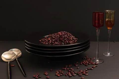 Still life of a stack of black plates with red beans, spoons and glasses of.. Stock Photos