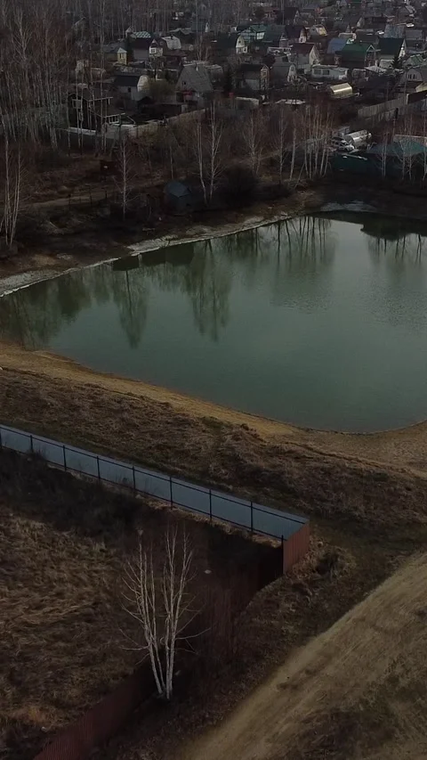 Still pond reflects bare trees and distant houses Stock-Footage 347499053