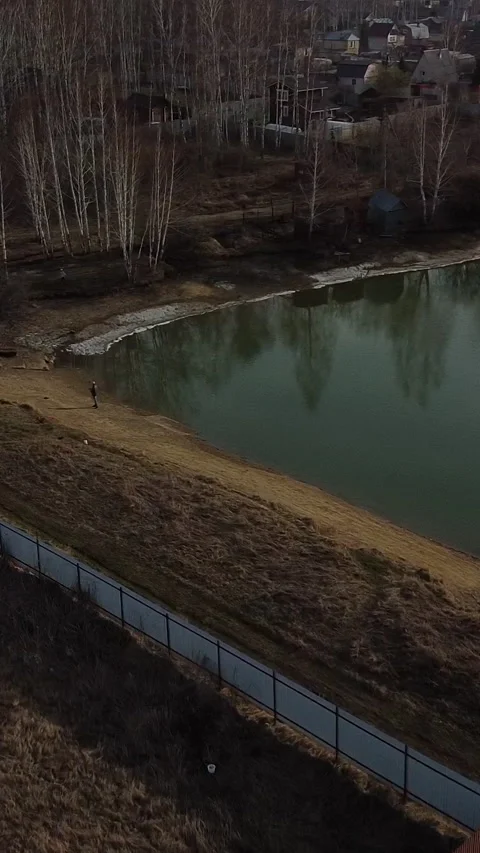 Still pond reflects bare trees and distant houses Stock Footage 347499074