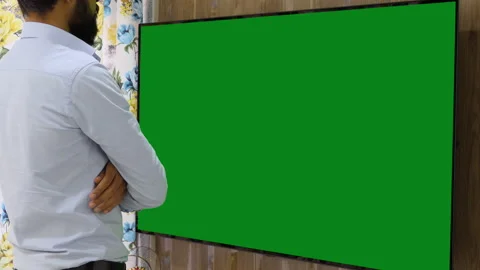 Still shot of a bearded indian man watching a large green chroma television Stock Footage 147408985