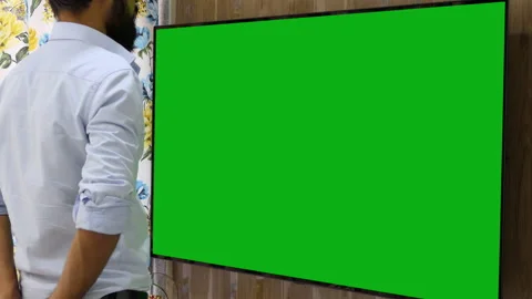 Still shot of a bearded indian man watching a large green chroma television Stock Footage 147409276