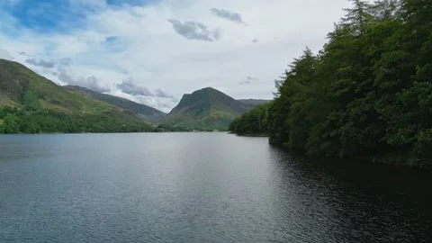 Still water mirrors distant green hills under a cloudy sky Stock Footage 345523344