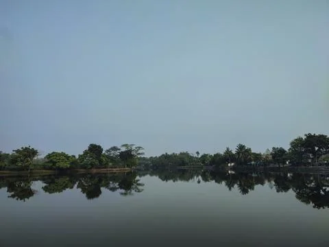 Still water mirrors trees lining calm riverbank Stock Photos