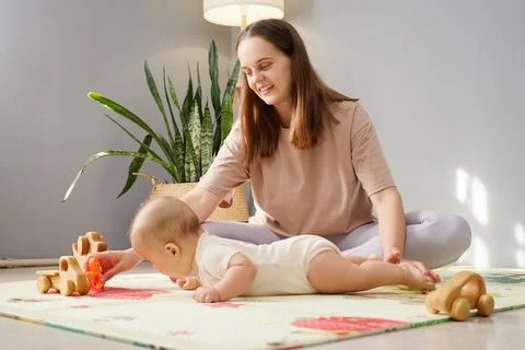 Stimulating infant body development. Smiling brown haired woman taking care o Stock Photos