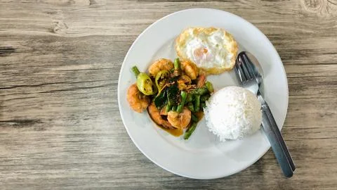 Stir-fried shrimp with chili paste over steamed rice on a white plate on a .. Stock Photos