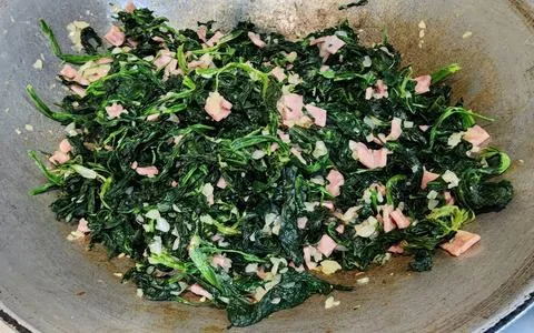 Stir-fried spinach with diced ham and minced garlic in a rustic metal wok. Stock-Fotos