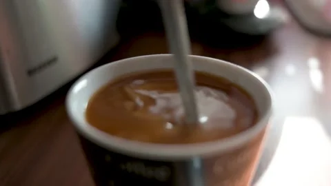 Stir a mug of coffee with a spoon to mix milk and sugar with the coffee Stock Footage 132282239