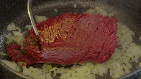 Stir raw ground beef meat dropped on top of diced onion in in gray frying pan Stock Footage 266783282