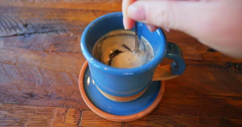 Stirring black coffee in a blue ceramic cup on a blue saucer on a brown wooden Stock Footage 230936170