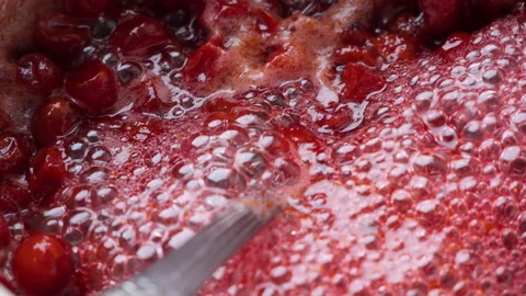 Stirring a bubbling red berry jam in a saucepan creates a mesmerizing slow Stock Footage 290467460