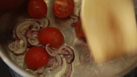 Stirring chopped onions with fresh cherry tomatoes on a frying pan Stock Footage 340551193