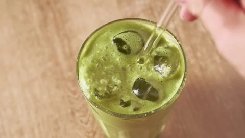 Stirring cold iced matcha green tea latte with glass straw in tall glass Stock Footage 345262050
