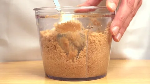Stirring crushed biscuits to prepare cake base in bowl with metal spoon Stock Footage 147307955