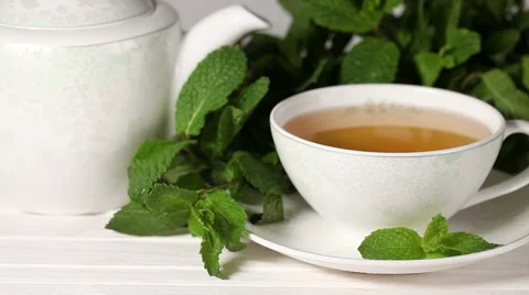 Stirring a cup of tea with mint in white mug on saucer Video stock 56027187