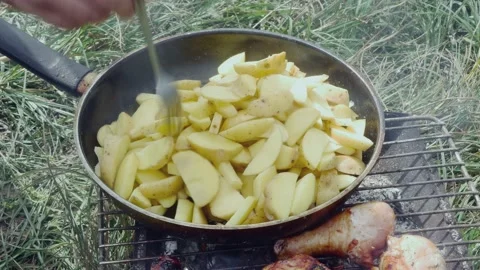Stirring with a fork still raw potatoes in a pan in a clearing Stock-Footage 213784325