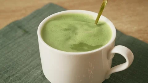 Stirring frothy green matcha latte with golden spoon in white ceramic mug. Stock Footage 345166366