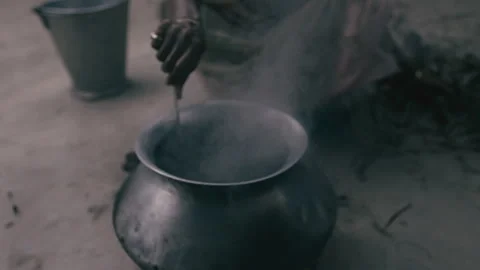 Stirring hot water over an open flame in a traditional cooking setting Stock Footage 321434347