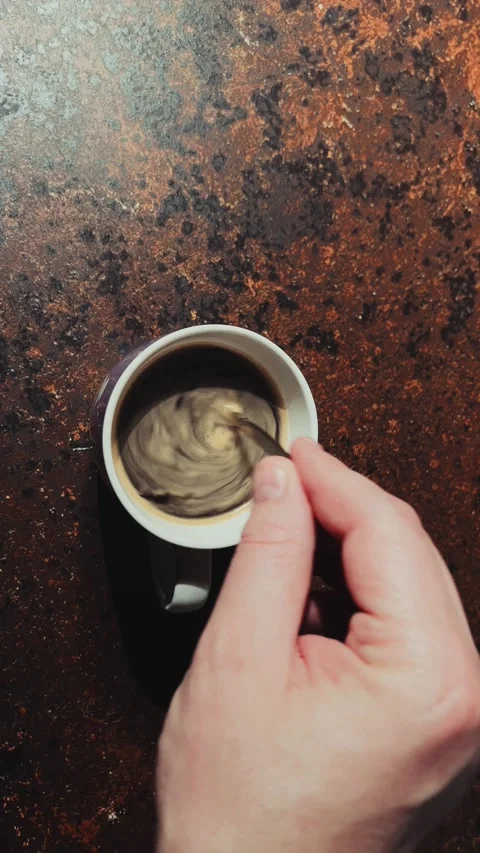Stirring instant coffee in white mug on brown table, vertical top view Stock Footage 334885165