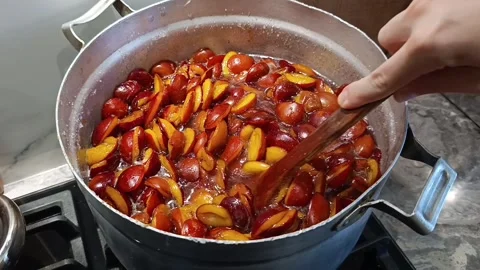 Stirring plum halves in boiling sugar syrup with wooden spoon for jam Stock Footage 344878359