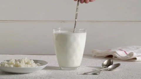 Stirring a probiotic kefir drink with a spoon, with kefir grains on a plate Stock Footage 169052012