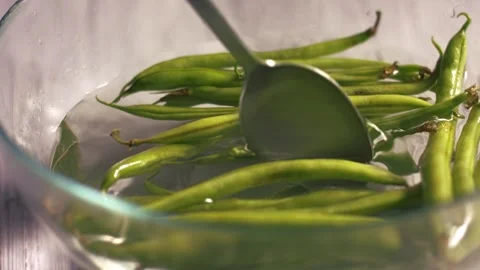 Stirring raw green beans floating in bowl of water Stock Footage 334108072