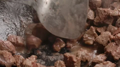 Stirring Sizzling Beef Chunks in a Pan with a Spatula Stock Footage 314111389