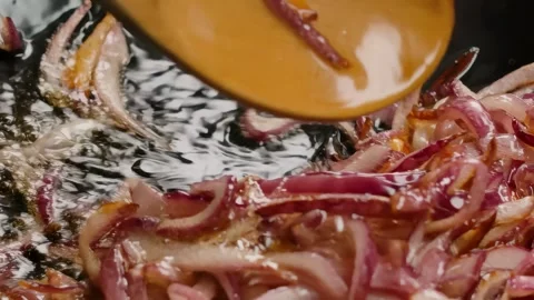 Stirring Sliced Red Onion in a Pan with a Wooden Spoon Stock Footage 312933055