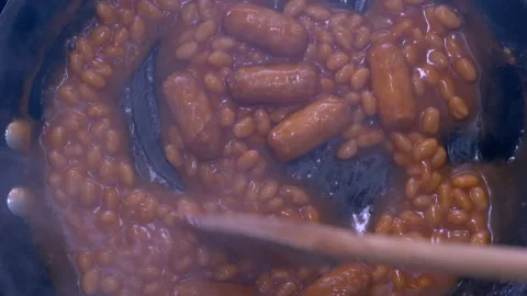 Stirring steaming hot baked beans and pork sausages in tomato sauce, in a pan. Stock-Footage 257086825