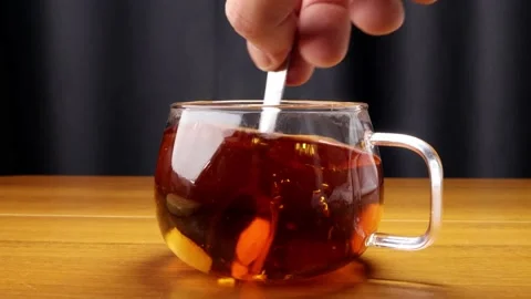 Stirring the sugars in the steaming hot tea in the glass mug with the spoon 스톡 동영상 184626647
