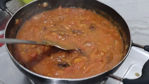 Stirring thick tomato curry chutney with a steel spoon in a frying pan on gas Stock Footage 127563532