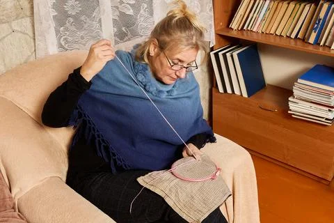Stitching pink thread, middle aged woman works with hoop on towel creating .. Foto stock