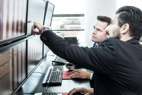 Stock traders looking at market data on computer screens. Businessmen trad... 写真素材