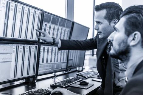 Stock traders looking at market data on computer screens. Businessmen trad... 写真素材