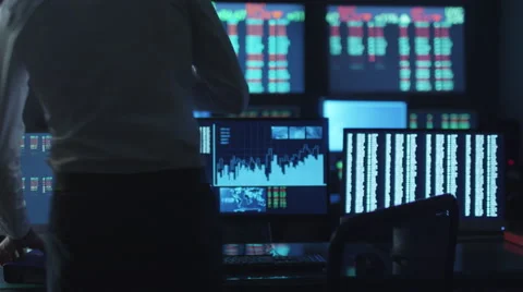 Stockbroker in white shirt is working in a dark monitoring room with displays Stock Footage