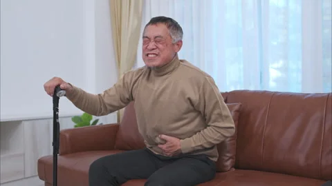 With a stomachache, a senior guy sits on a sofa with a walking stick Stock Footage 260678857