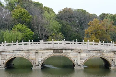 Stone Arch Bridge Over Calm Park Lake Surrounded by Lush Trees and Autumn Stock Photos
