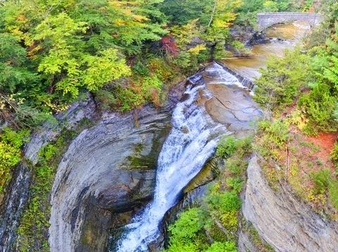 Stone arch bridge over river leading to huge waterfall into gorge 写真素材
