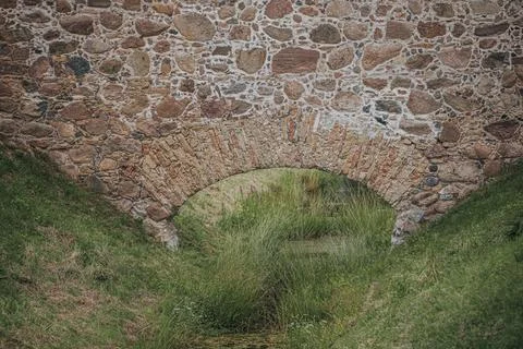 Stone arch bridge over a small stream surrounded by lush green grass and ve.. Stock Photos
