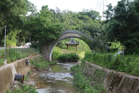 The stone arch bridge over the stream is located in shenzhen nanshan park Stock Photos