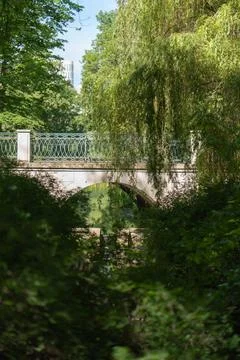 Stone arch bridge with patterned railing hidden behind willow tree in park Stock Photos