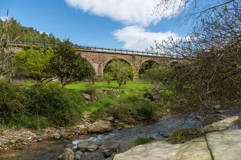 Stone arch bridge spanning river with green landscape Stock Photos