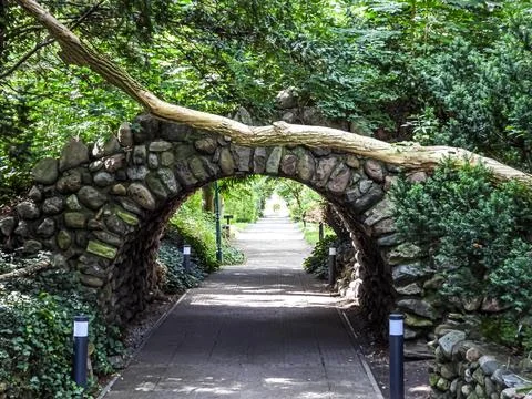 Stone archway with fallen tree branch over a garden path in summer Stock Photos