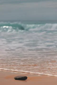 Stone on the beach with blue waves in the background 스톡 사진