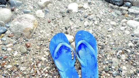 Stone beach with pair of blue slippers and waves move them. Top view. Stock Footage 118974522
