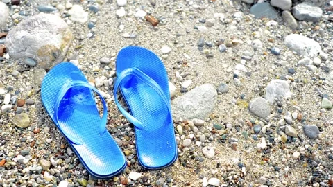 Stone beach with pair of blue slippers and waves move them. Top view. Video stock 118975111