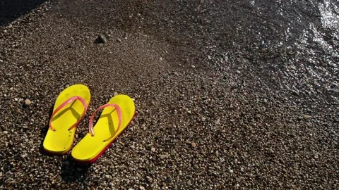 Stone beach with pair of yellow slippers and waves move them. Top view. Stock Footage 118968039