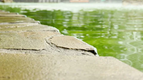 Stone border frames a rippling green fountain pool 動画素材 336363562