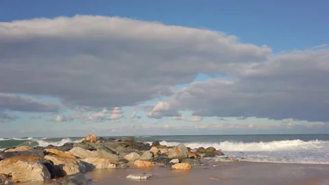 Stone breakwaters. sandy beach. blue sky. Large sea waves with white foam Stock Footage 144108489